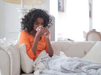 Young girl wrapped in blankets blowing her nose