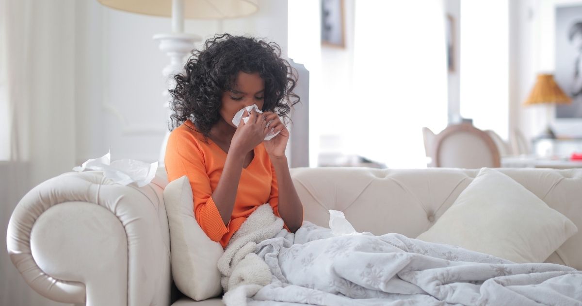 Young girl wrapped in blankets blowing her nose