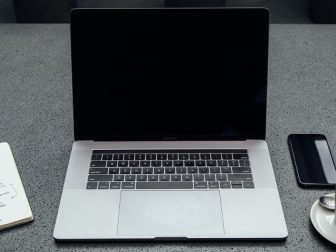 Turned-off MacBook Pro between cup of coffee, iPhone, notebook, and pen