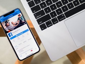 Mobile Facebook app on an iPhone next to a MacBook on a table