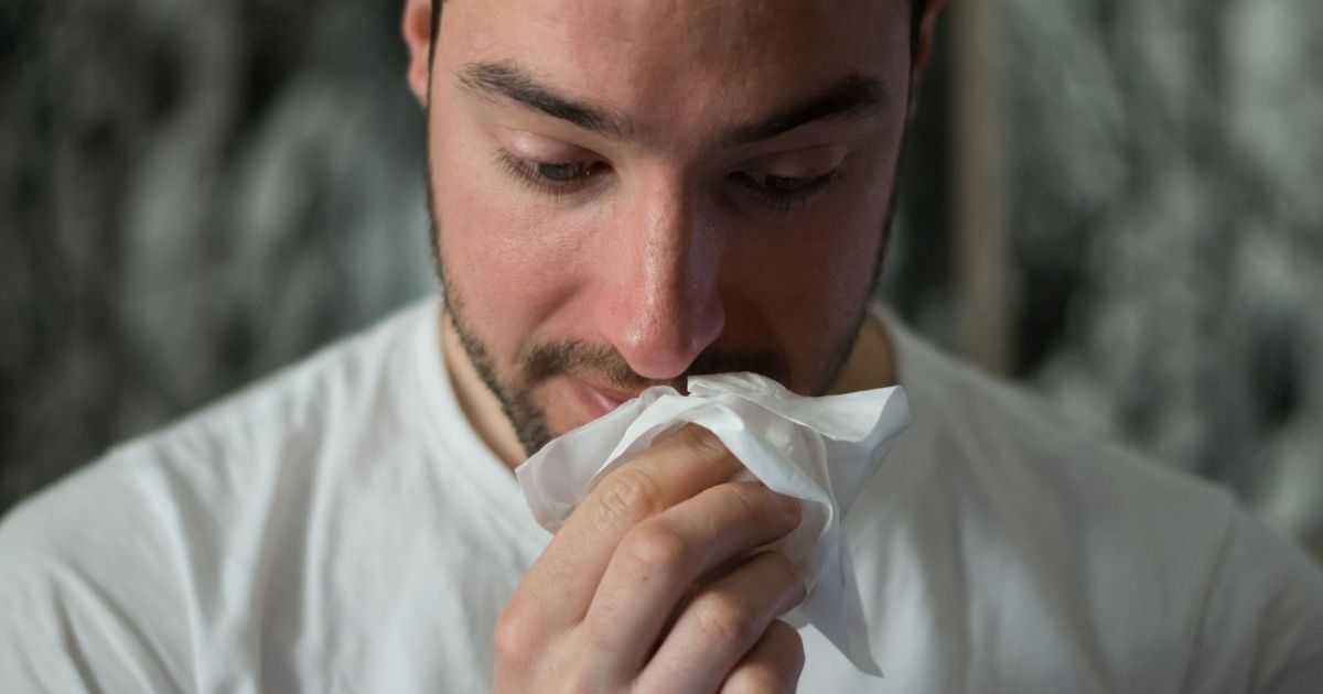 Man wiping nose with a tissue