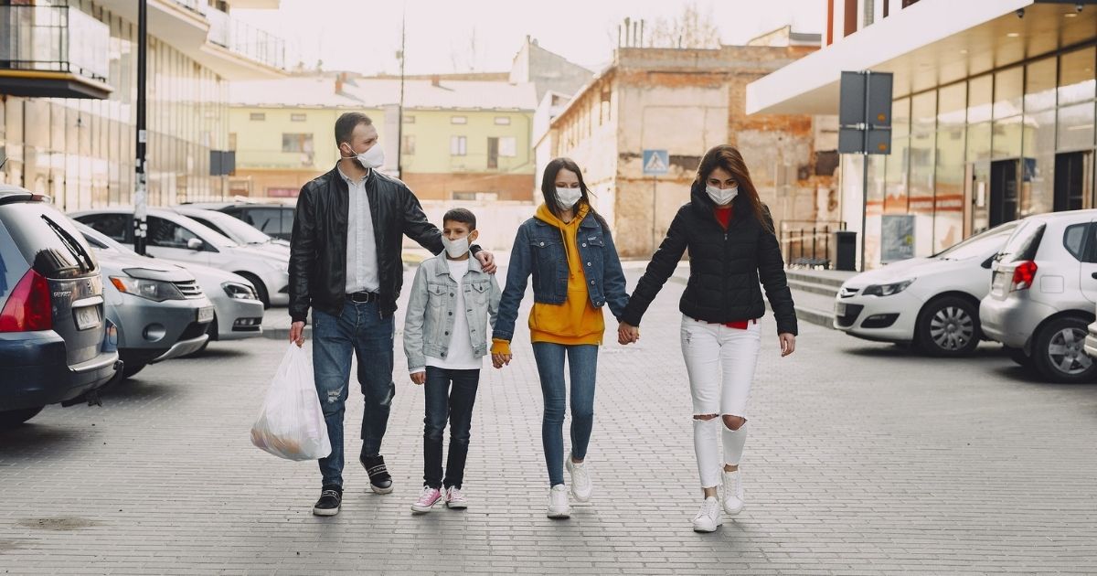 Family in medical masks walking along parking