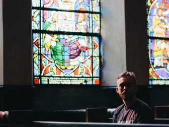 Man sitting in church pew backed by stained glass windows