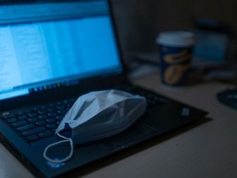 Black laptop computer with a disposable face mask on the keyboard