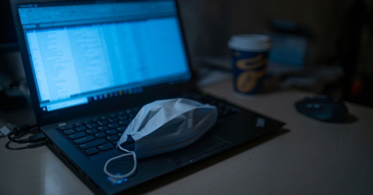 Black laptop computer with a disposable face mask on the keyboard