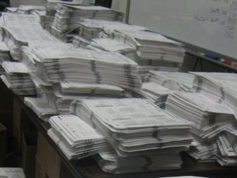 A stack of voter ballots lay on a table ready to be scanned and counted.