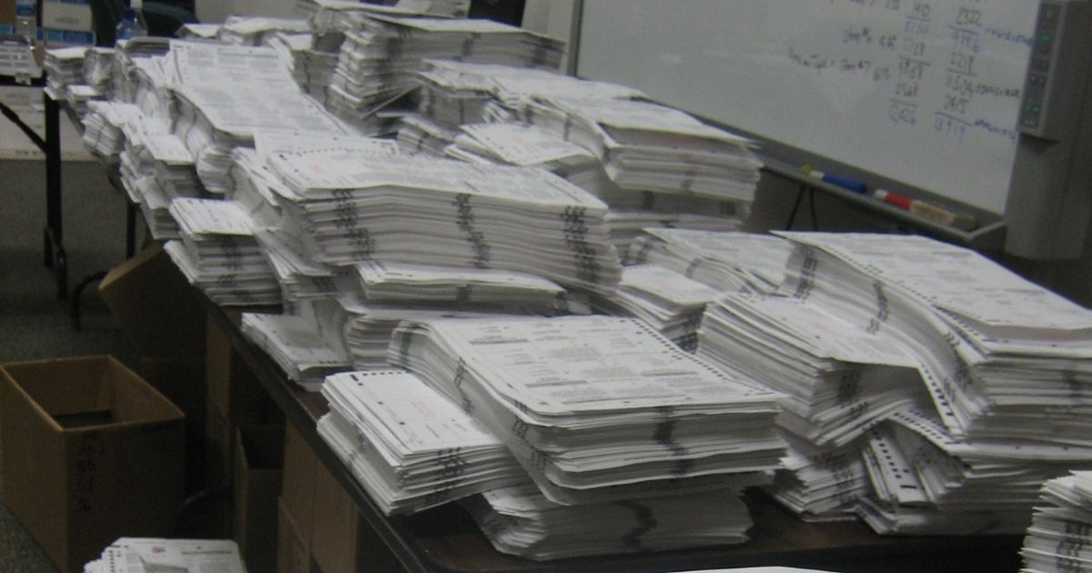 A stack of voter ballots lay on a table ready to be scanned and counted.