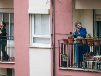 People standing on apartment balconies in lockdown.