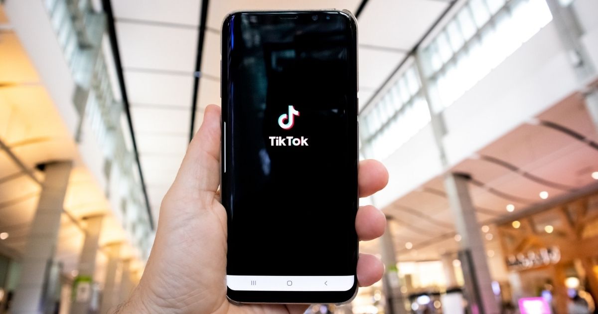 Person holding a smartphone displaying a Tik Tok splash screen.