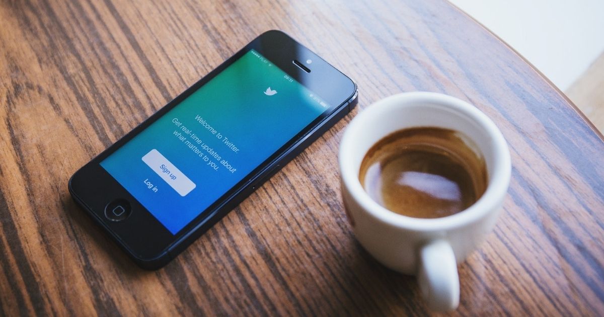 Phone on a table with the Twitter login screen next to a cup of coffee