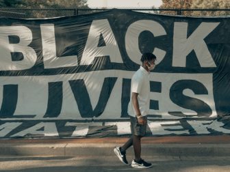 Man walks in front of a Black Lives Matter flag