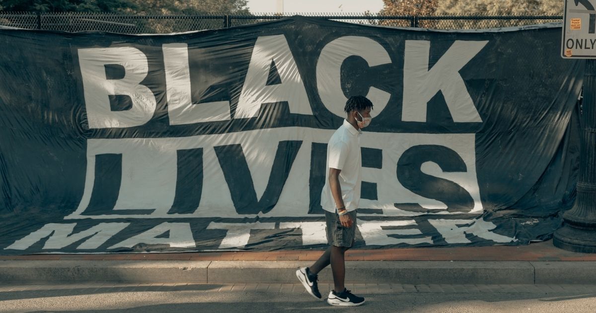 Man walks in front of a Black Lives Matter flag