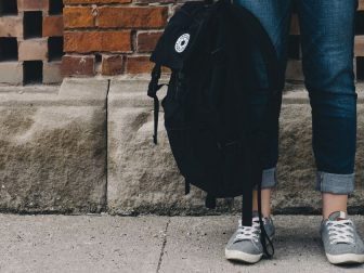 Student standing against a brick wall with a backpack in hand