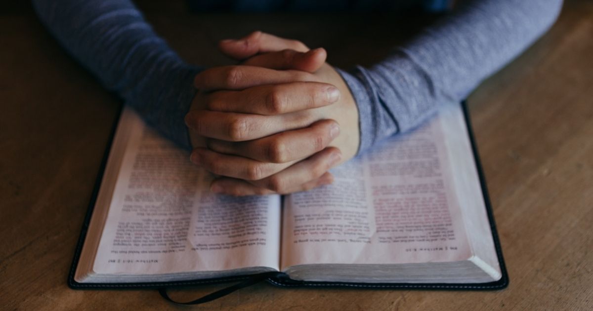 Man's clasped hands on an open bible