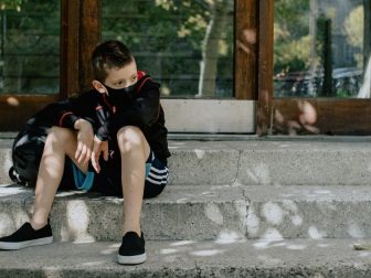 boy with mask on on the steps waiting for school