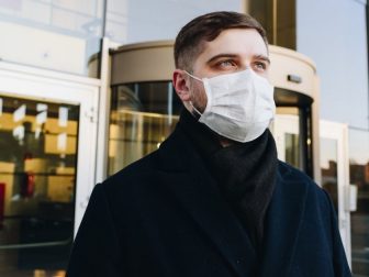 Man, young professional, outside his office during coronavirus COVID-19 outbreak and pandemic wearing a face mask