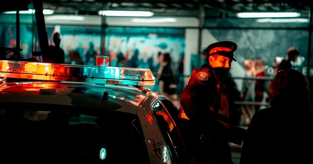 Police officer standing beside his squad car with the lights on