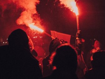 Hooded people holding roman candles at a night riot.