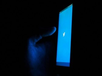 Hand holding a phone displaying the Twitter splash screen in the dark