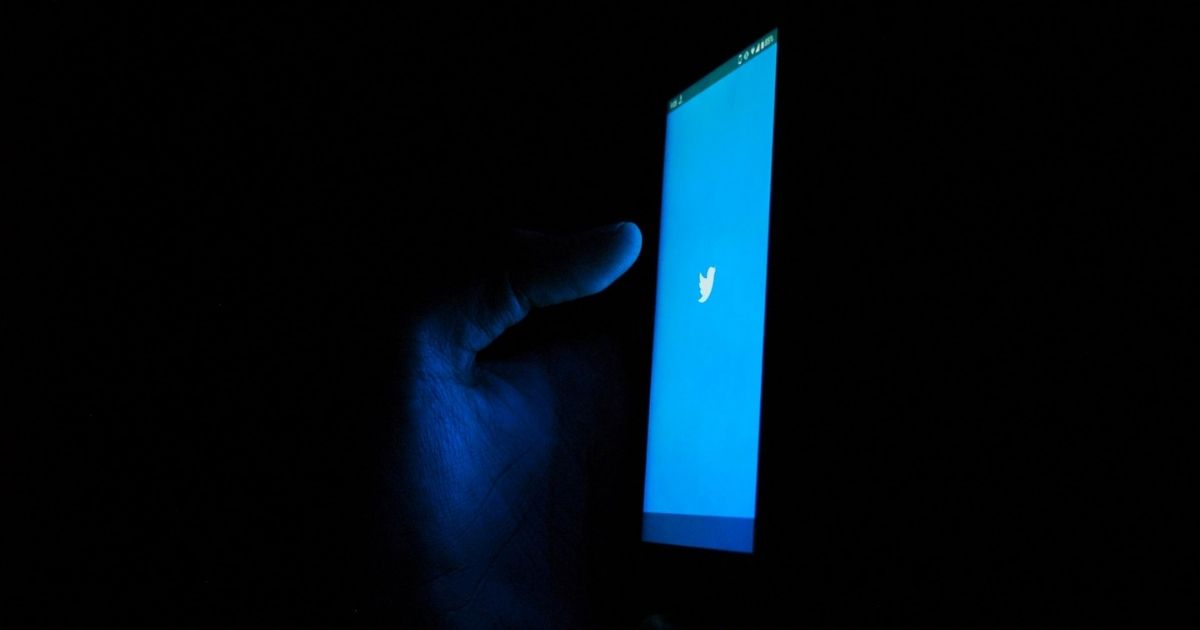 Hand holding a phone displaying the Twitter splash screen in the dark