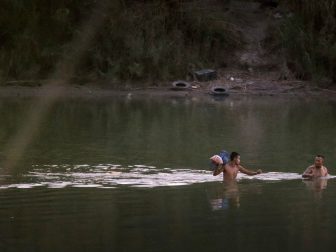 Led by a guide, right, an illegal alien carriers his belongings in a plastic bag as he wades across the Rio Grande as night falls near Eagle Pass, Texas, June 20, 2019. Within approximately 45 minutes he was apprehended by U.S. Border Patrol agents. His guide was spotted returning to the Mexico side of the river after delivering his client to U.S. soil. CBP photo by Glenn Fawcett