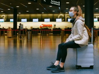 Girl in mask sitting on a suitcase in an airport