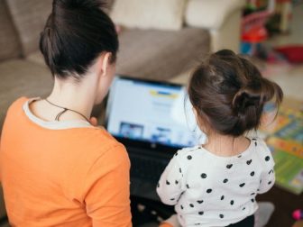 Mom teaches daughter for work on laptop.
