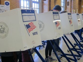 Voters are pictured behind voting booths, filling in ballots to be cast.