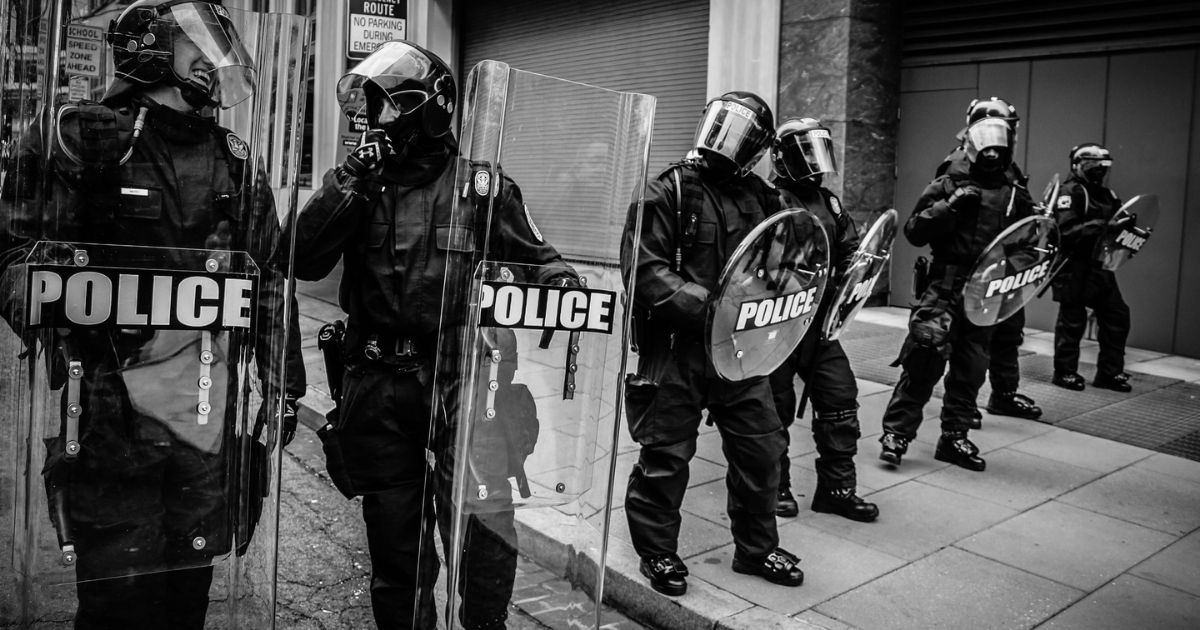 Riot police waiting on a city street sidewalk