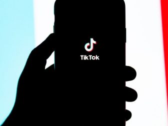 Silhouette of a hand holding a phone with the Tik Tok splash screen