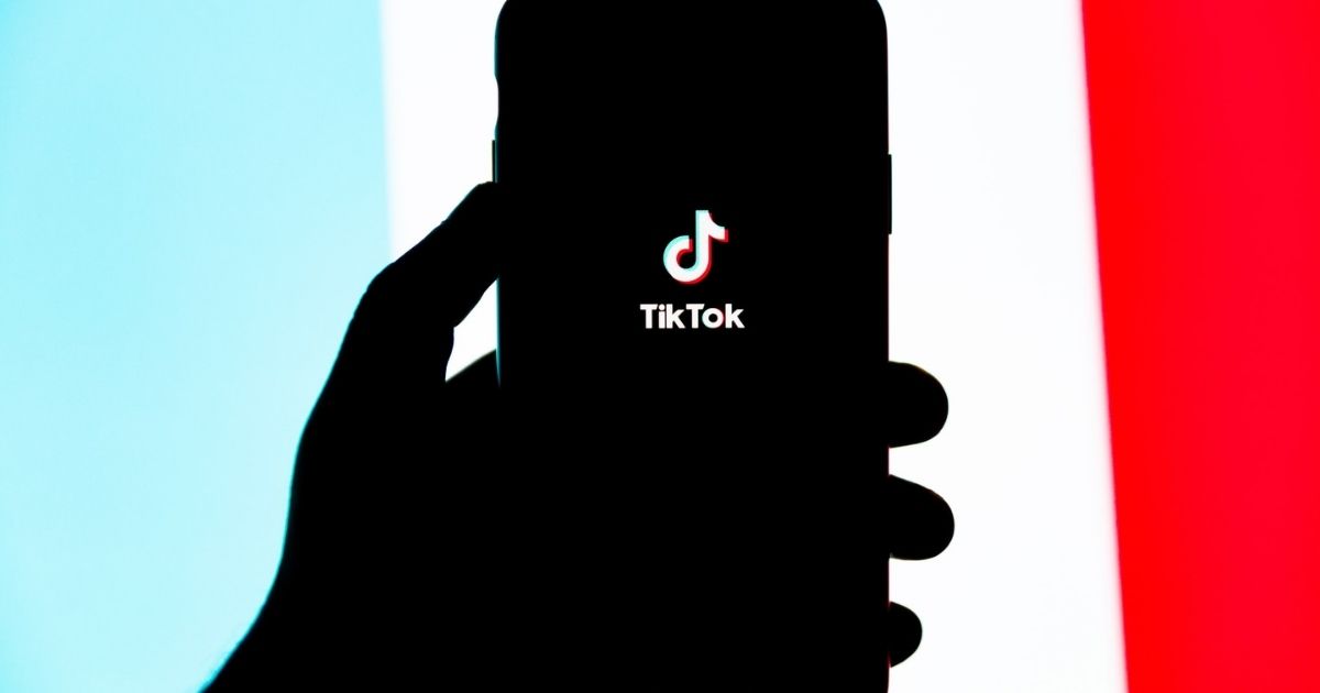 Silhouette of a hand holding a phone with the Tik Tok splash screen