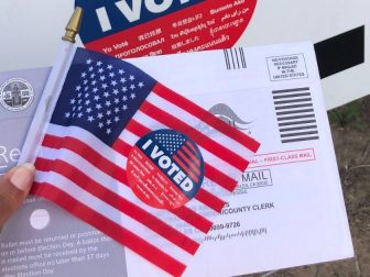 Person holding a mail-in ballot and a miniature American flag