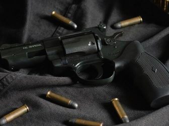 A black revolver on black cloth, with ammunition