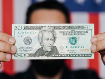 Person holding a $20 bill in front of an American flag