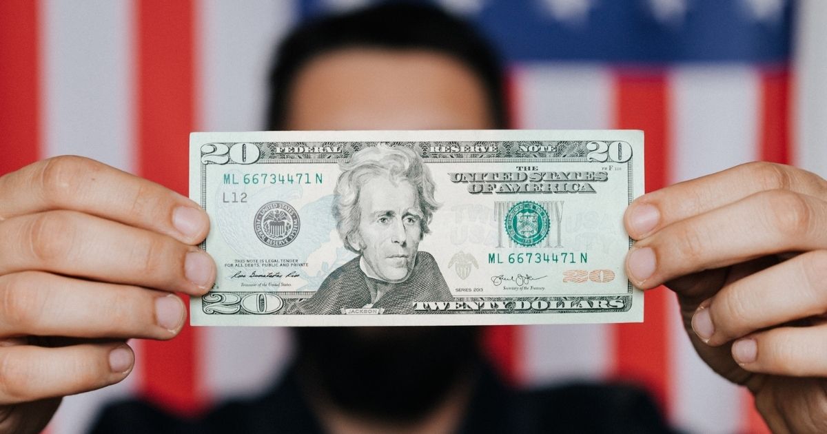 Person holding a $20 bill in front of an American flag