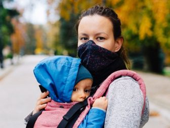 Woman outside wearing a mask and carrying a child