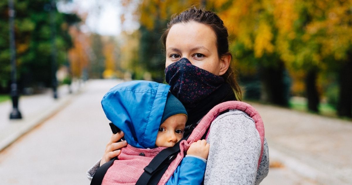 Woman outside wearing a mask and carrying a child