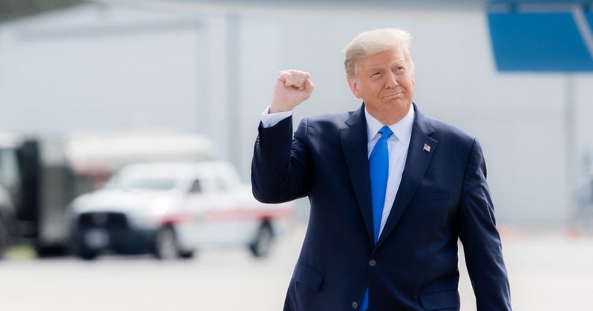 President Donald J. Trump gestures with a fist pump as he walks across the tarmac.