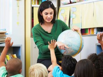 Female teacher holds globe while teaching students.