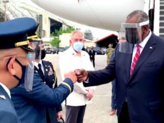 Secretary of Defense Lloyd Austin wears a face mask and a visor when greeting individuals in 2021.
