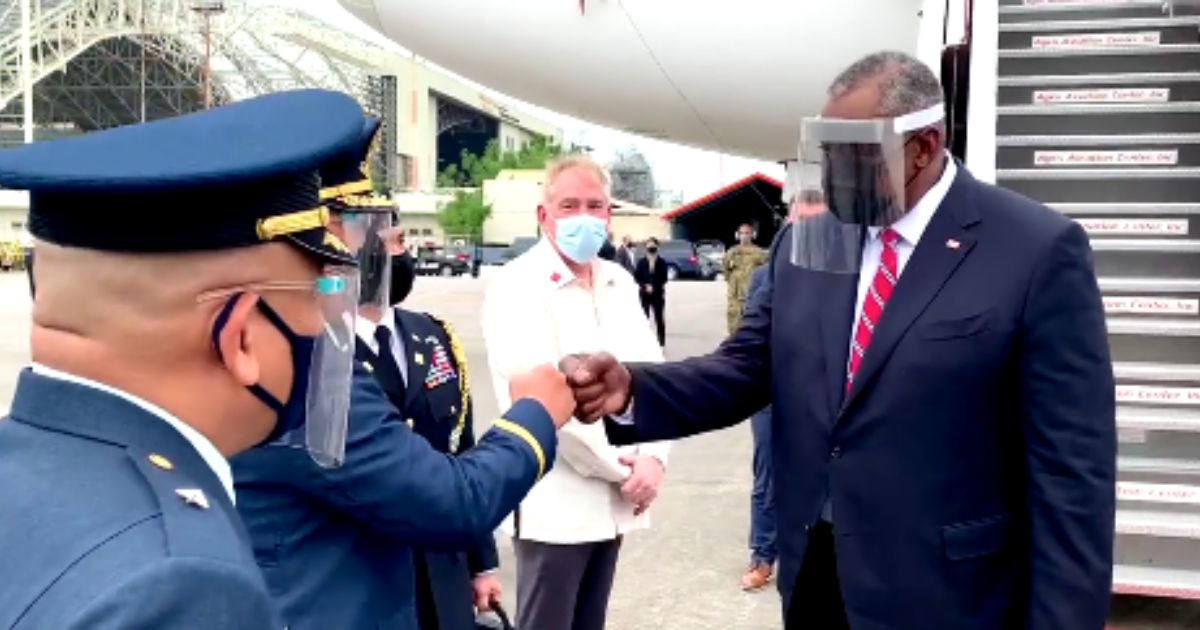 Secretary of Defense Lloyd Austin wears a face mask and a visor when greeting individuals in 2021.