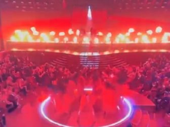 A scene from the Grammys shows dancers suffused in red lighting with fire flaring on stage.