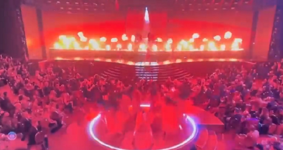 A scene from the Grammys shows dancers suffused in red lighting with fire flaring on stage.