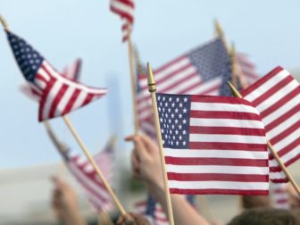 A crowd waves American flags in the above stock image.