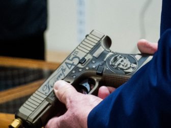 A closeup of former President Donald Trump's hands holding a Glock handgun his likeness on it.