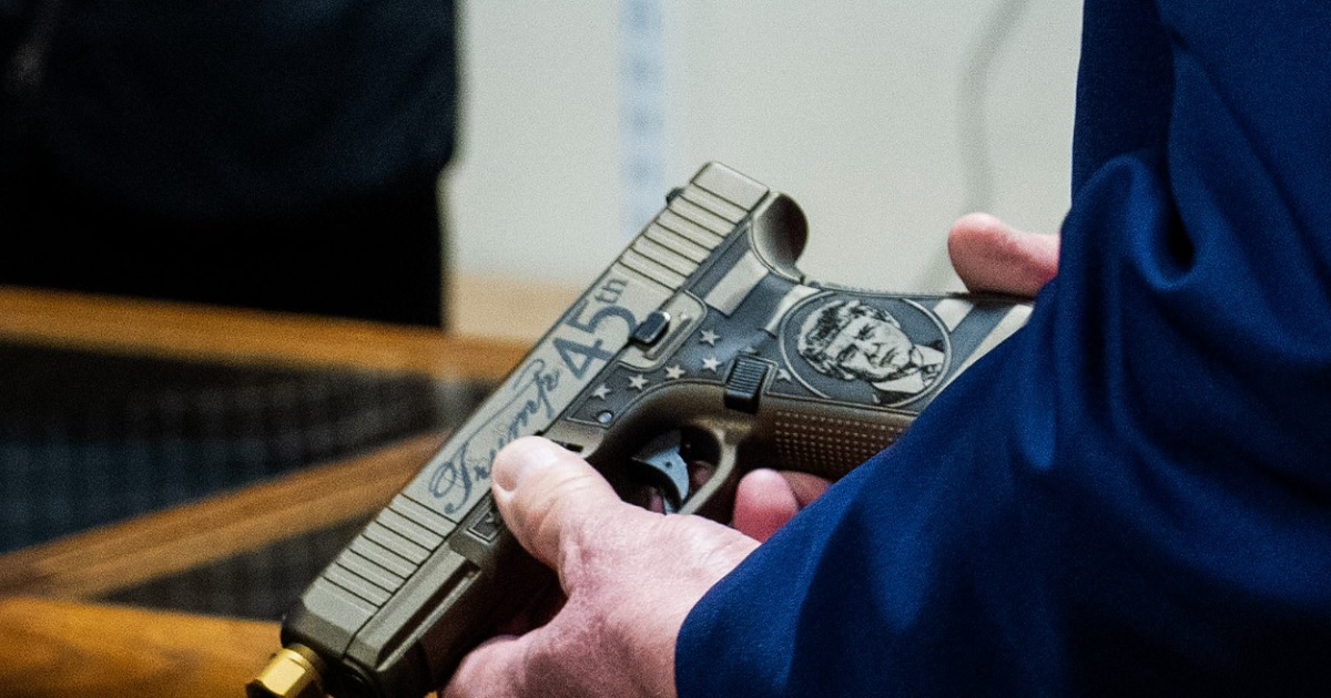 A closeup of former President Donald Trump's hands holding a Glock handgun his likeness on it.