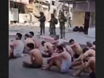 Prisoners sat on the street, stripped to their underwear, as they waited to be loaded onto truck.