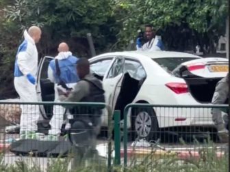 Investigators examine one of the carjacked vehicles used in the attack while armed soldiers stand by.