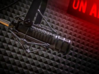 This image shows a professional microphone in a radio station studio with an on air sign.